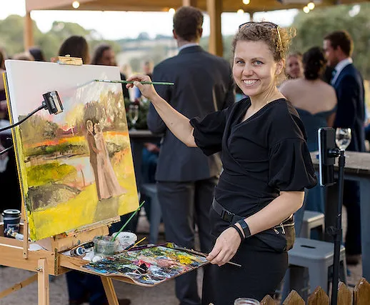 Olga smiling beside her easel at a wedding